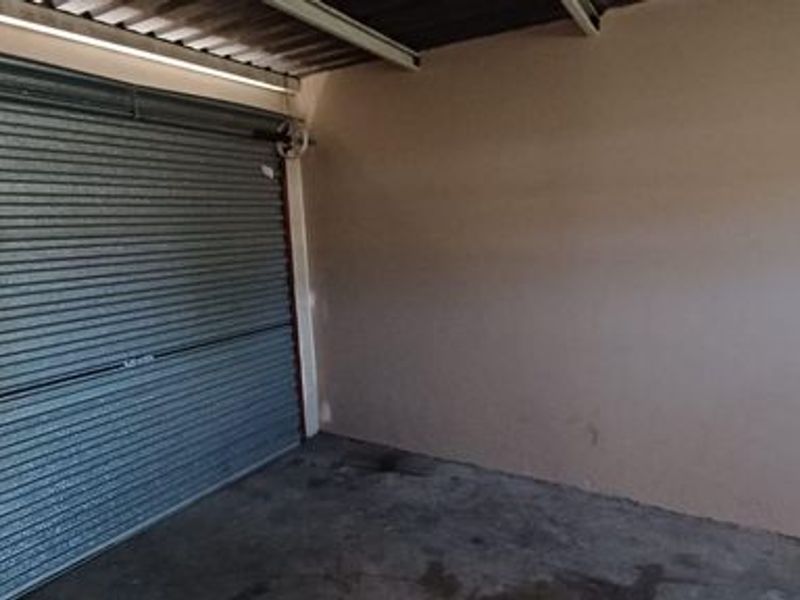 A functional, empty single-car garage featuring a metal roller shutter door, concrete flooring, and a wall-mounted electrical outlet.