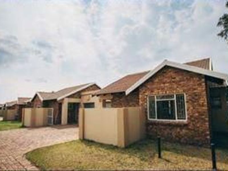Front elevation of a face-brick townhouse complex featuring paved driveways, tiled roofs, and secure boundary walls.