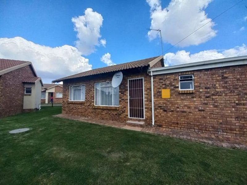 Rear view of a face brick townhouse featuring a tiled roof, security gate, and a well-maintained lawn area.