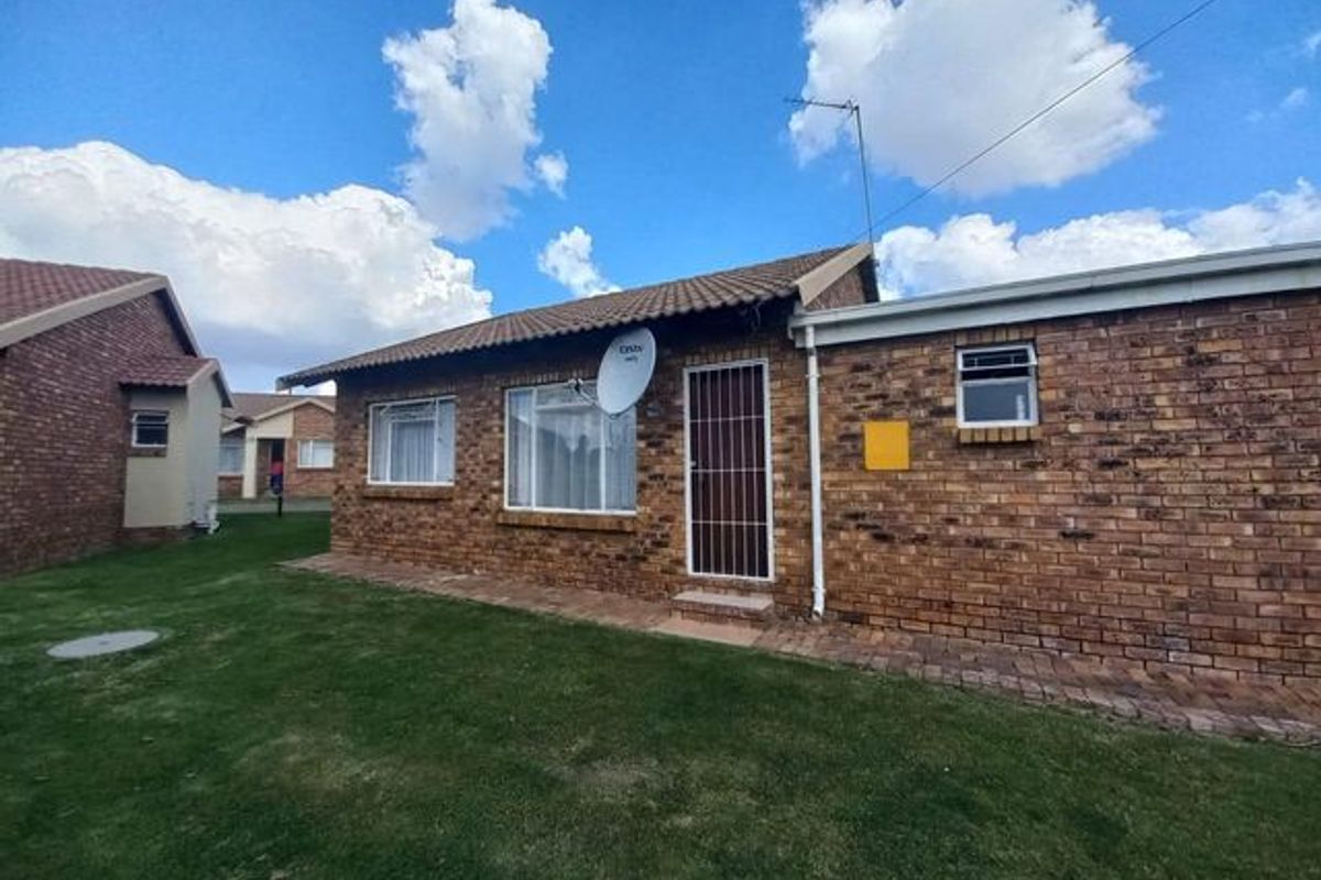 Rear view of a face brick townhouse featuring a tiled roof, security gate, and a well-maintained lawn area.