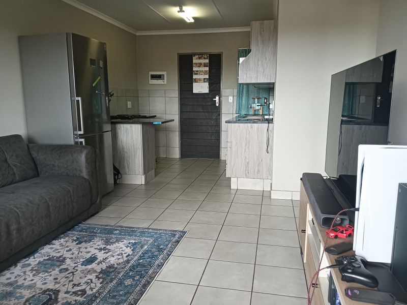 An open-plan living and kitchen area featuring tiled flooring, modern wood-look cabinetry, and a functional kitchen layout with built-in appliances.