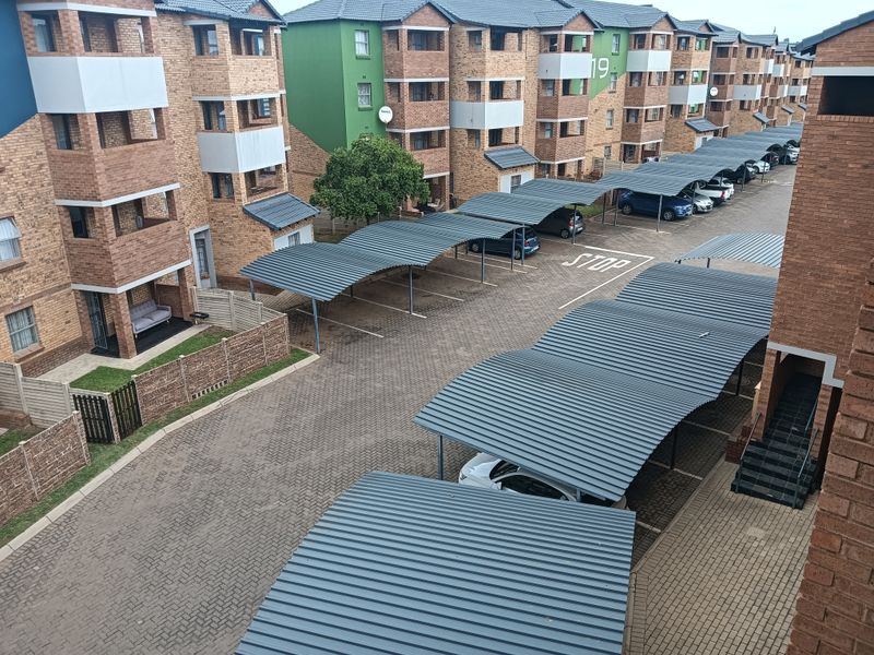 An elevated aerial view of an apartment complex featuring brick buildings, covered parking bays, and paved driveways.