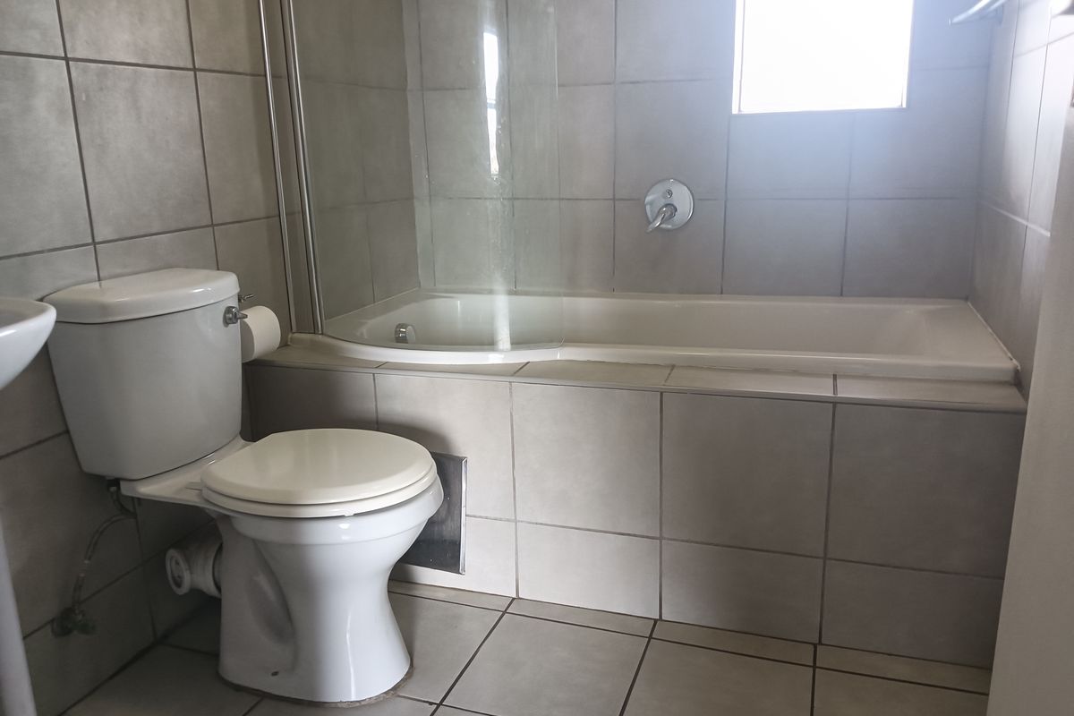 A functional bathroom featuring a built-in bathtub with a glass shower screen, ceramic tiling throughout, and a standard toilet.