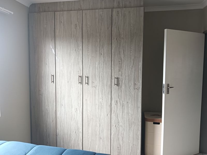 A bedroom featuring modern wood-grain finish built-in cupboards with metal handles and a standard internal door.