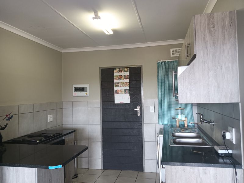 A functional kitchen featuring modern grey wood-look cabinetry, black countertops, a double sink, and a built-in electric hob with tiled splashbacks.