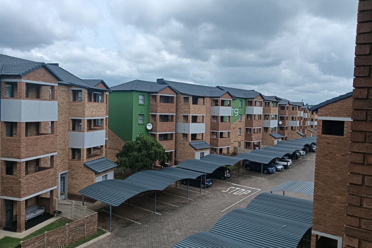An elevated view of a residential apartment complex featuring face brick buildings, tiled roofs, and extensive covered parking facilities within a paved courtyard.