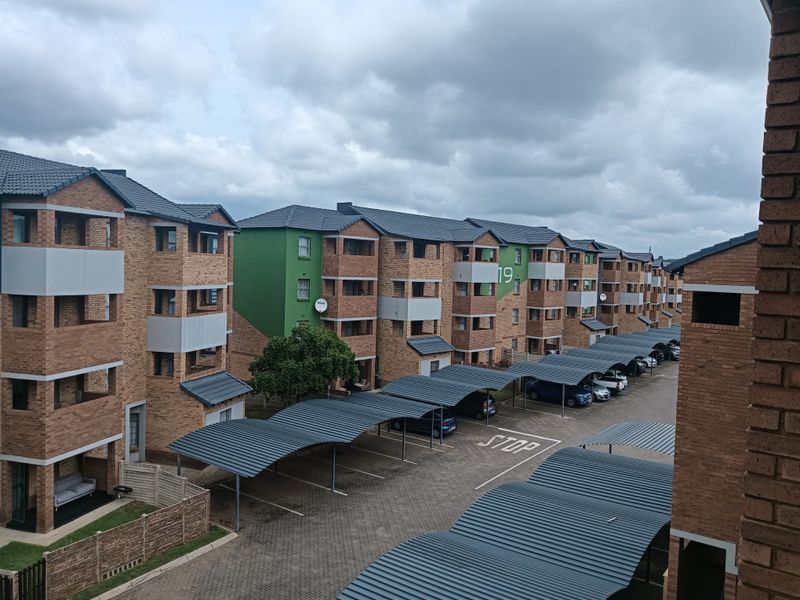 An elevated view of a residential apartment complex featuring face brick buildings, tiled roofs, and extensive covered parking facilities within a paved courtyard.