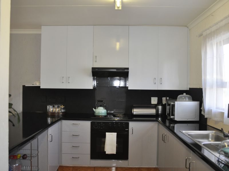 A functional U-shaped kitchen featuring white upper cabinetry, black countertops, a built-in oven, and a black extractor fan.