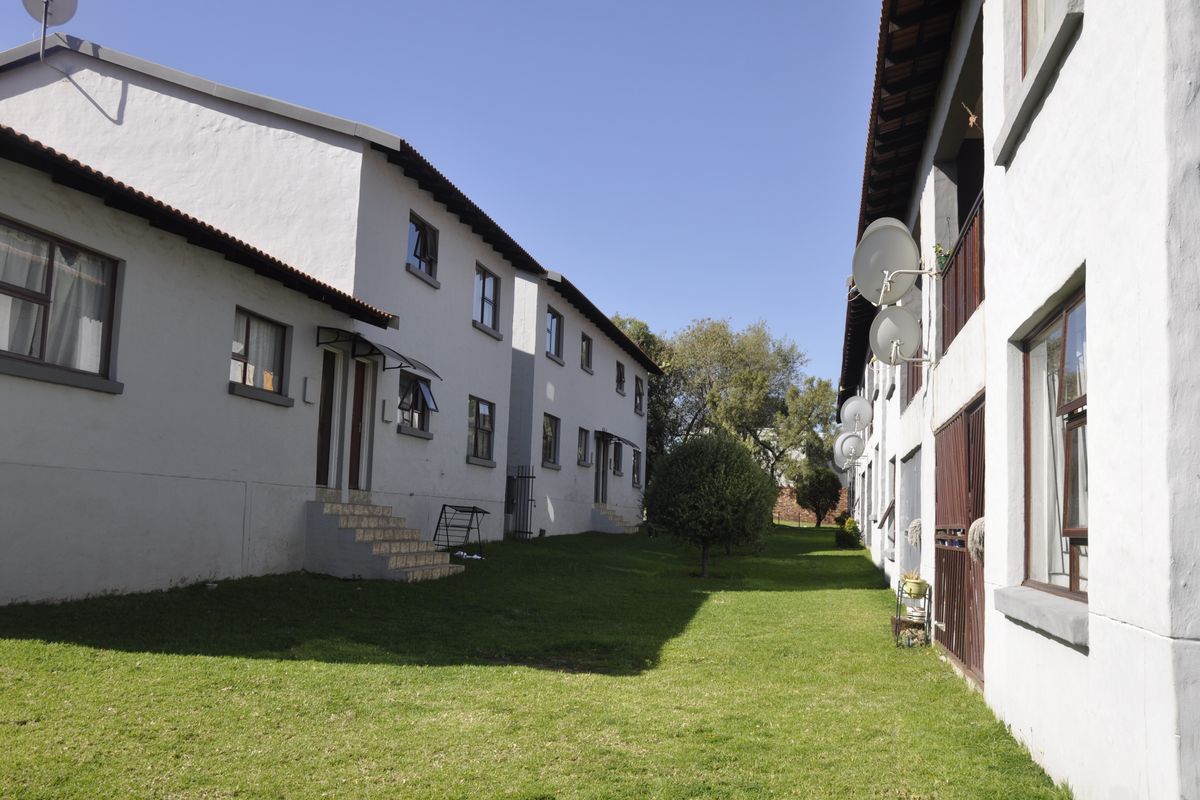 Exterior view of apartment complex buildings featuring white rendered facades, tiled roofs, and a shared central lawn area.