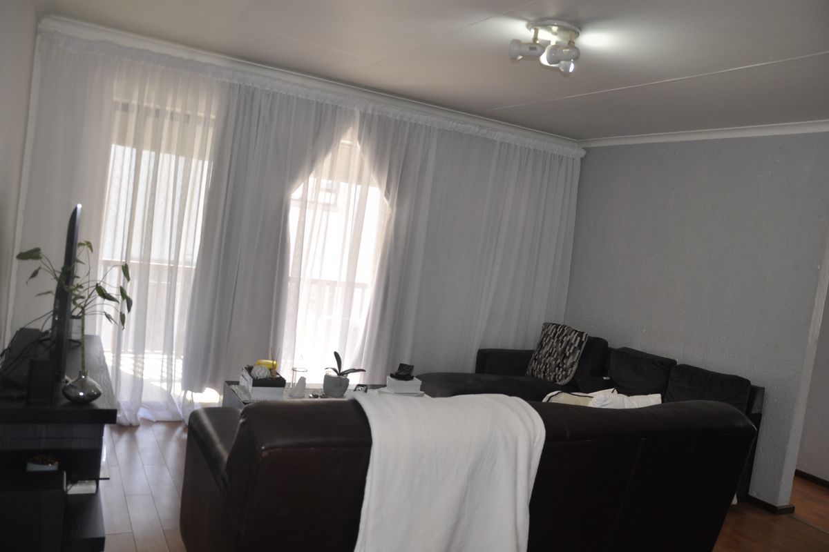 A comfortable living room featuring laminate flooring, neutral walls, and large sliding glass doors with sheer curtains providing access to a balcony.