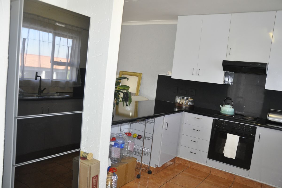 A functional kitchen featuring white upper cabinetry, dark countertops, a built-in oven with extractor fan, and tiled flooring.