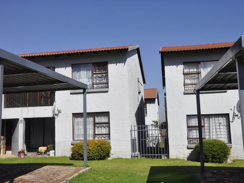 Exterior view of a multi-story apartment complex featuring tiled roofs, metal carports, and paved driveway areas with established garden landscaping.