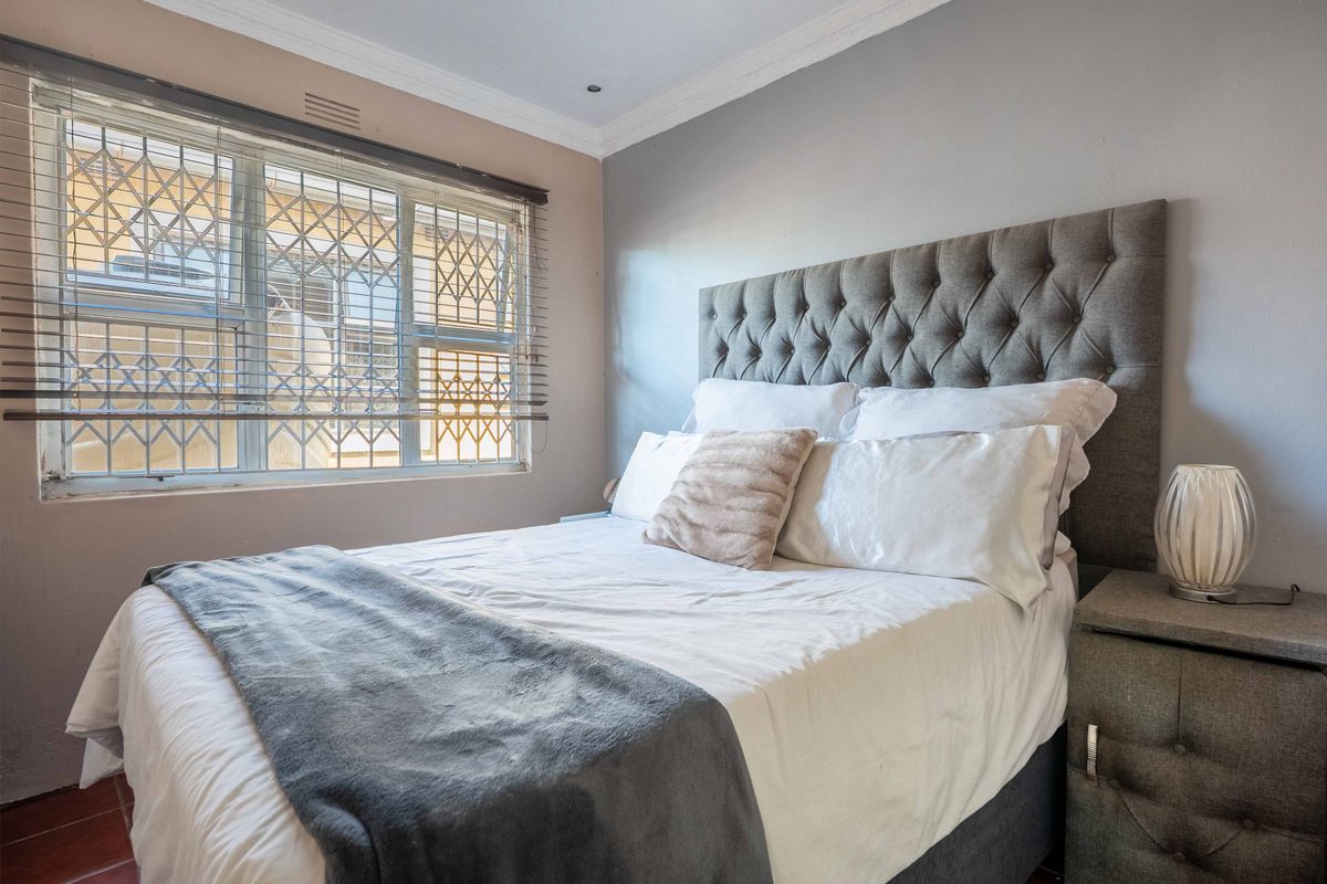 A cozy bedroom featuring a window with security bars, crown molding, and neutral wall finishes.