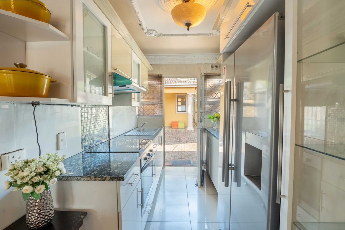 A galley-style kitchen featuring granite countertops, built-in cabinetry, a glass-top hob, and an integrated extractor fan, leading directly to an outdoor patio area.