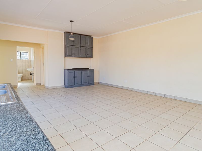 Spacious open-plan kitchen and living area featuring tiled flooring, granite countertops, and built-in cabinetry, with an adjacent bathroom visible.