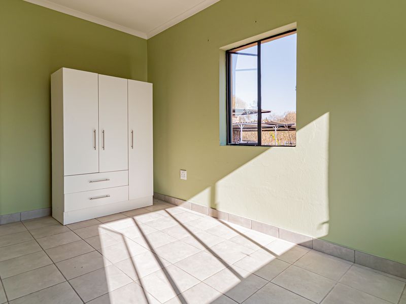 A bright, empty bedroom featuring tiled flooring, green painted walls, and a built-in wardrobe, offering a clean and neutral space.
