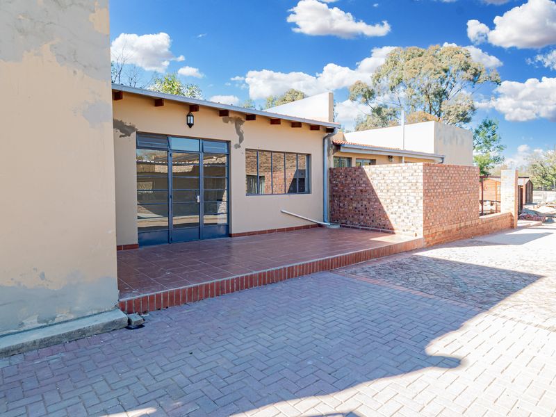 Rear exterior view featuring a tiled patio, brick walling, and paved driveway area with visible maintenance required on the exterior plaster and paintwork.