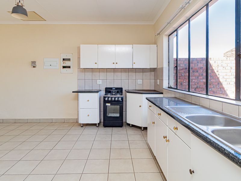 A functional, empty kitchen featuring white cabinetry, a gas stove, double basin sink, and tiled flooring, offering a clean canvas for potential updates.