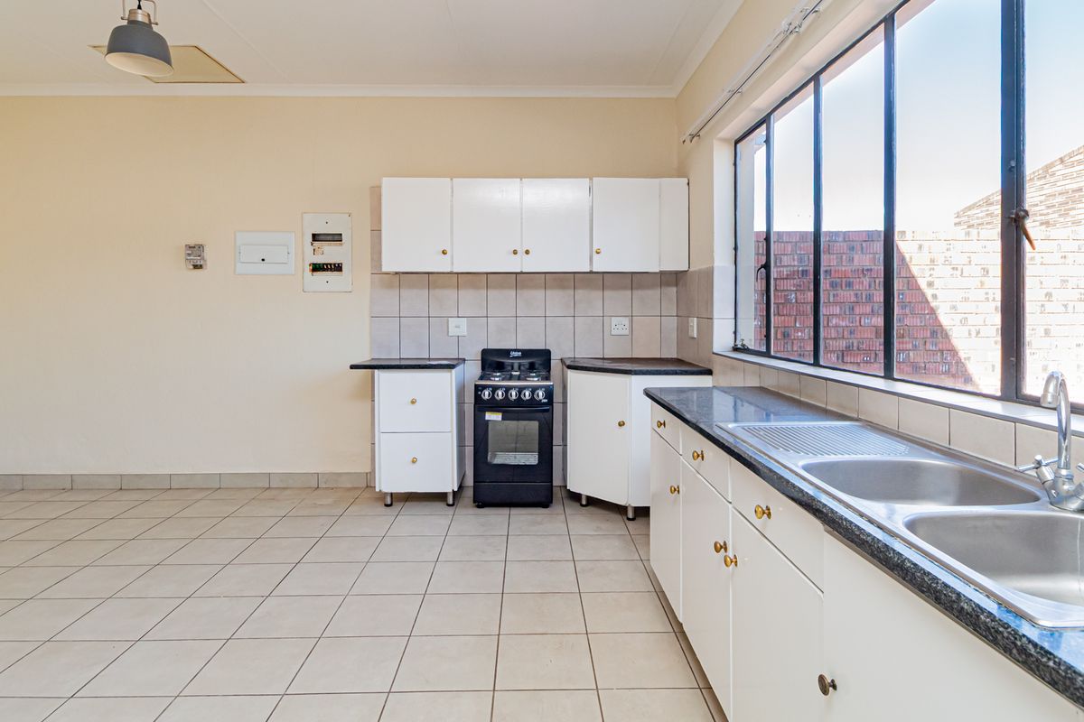 A functional, empty kitchen featuring white cabinetry, a gas stove, double basin sink, and tiled flooring, offering a clean canvas for potential updates.