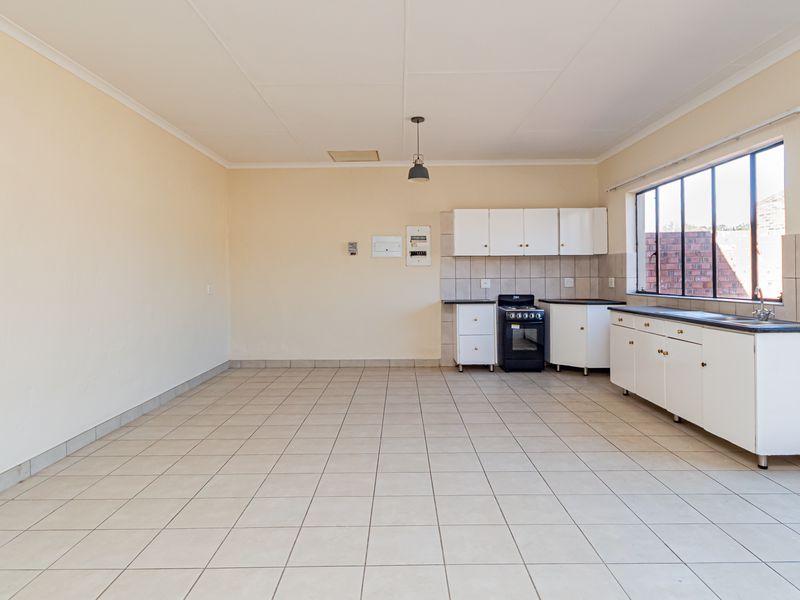 A spacious, empty kitchen featuring tiled flooring, white built-in cabinetry, a freestanding stove, and a double sink with a tiled backsplash.