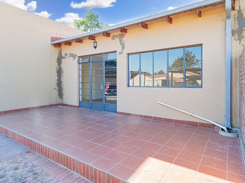 A covered outdoor patio area featuring tiled flooring, exposed timber rafters, and steel-framed windows, requiring some exterior maintenance and cosmetic attention.