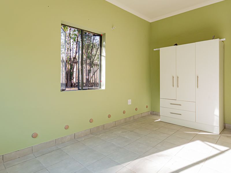 A bright, empty bedroom featuring light green walls, tiled flooring, and a built-in white wardrobe.