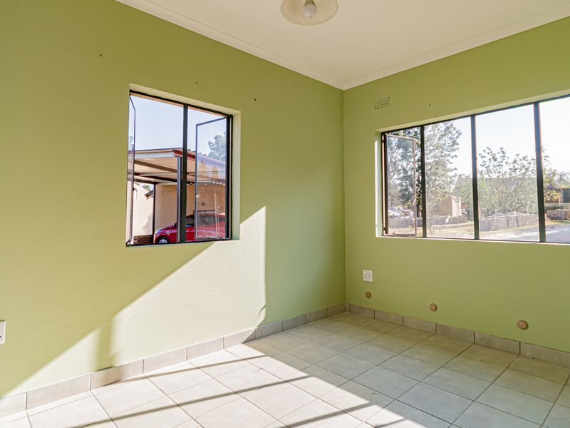 A bright, empty bedroom featuring tiled flooring, large steel-framed windows, and neutral green walls, offering a clean canvas for personalization.