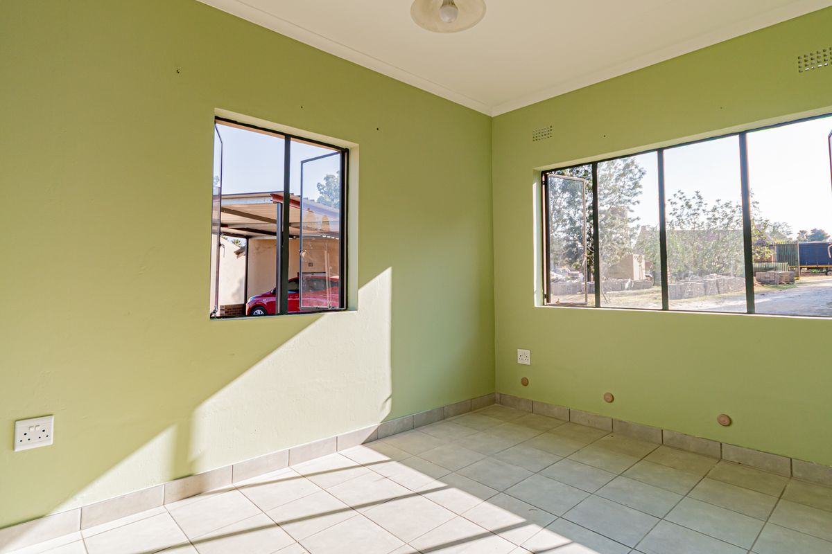 A bright, empty bedroom featuring tiled flooring, large steel-framed windows, and neutral green walls, offering a clean canvas for personalization.