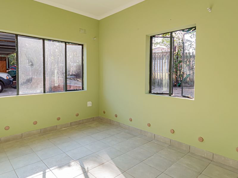 An empty living room featuring light green walls, tiled flooring, and large windows providing natural light and views of the exterior.