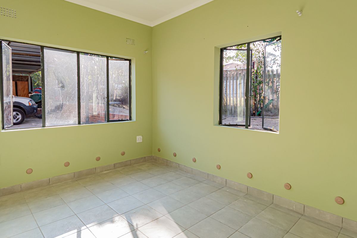 An empty living room featuring light green walls, tiled flooring, and large windows providing natural light and views of the exterior.
