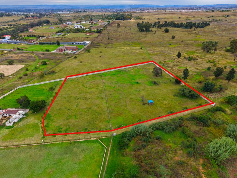 Aerial view of a vacant residential plot with clear boundary markings, situated in a developing semi-rural area.
