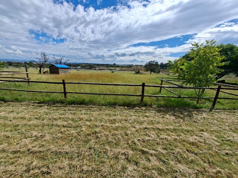 A wide view of a vacant residential plot featuring established timber post and rail fencing and a small wooden storage shed.