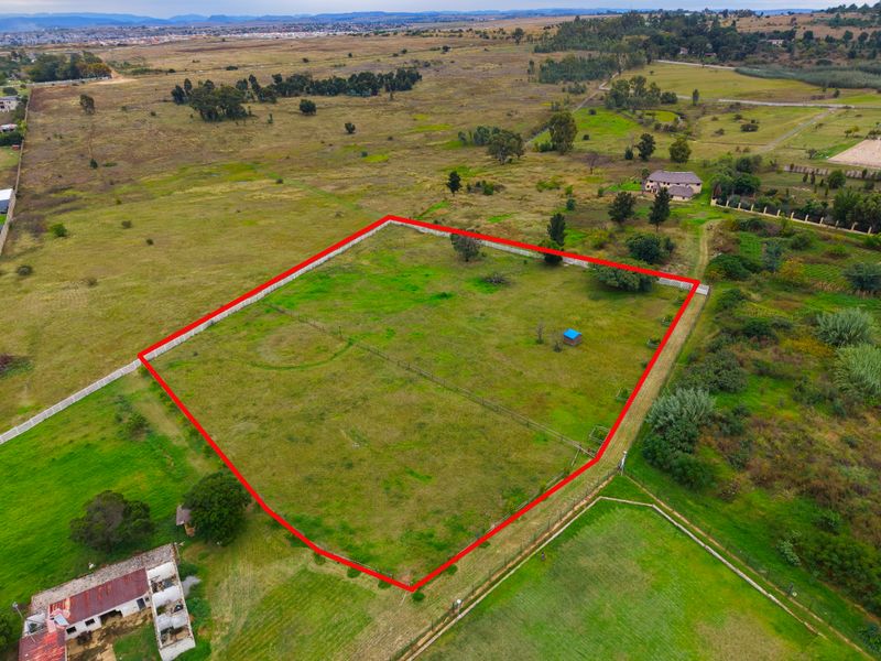 Aerial view of a vacant residential plot featuring perimeter fencing and boundary walls, situated in a semi-rural landscape.
