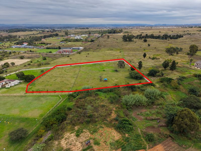 Aerial view of a vacant residential plot featuring perimeter fencing and open grass land in a developing suburban area.