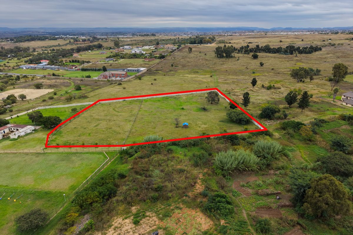 Aerial view of a vacant residential plot featuring perimeter fencing and open grass land in a developing suburban area.