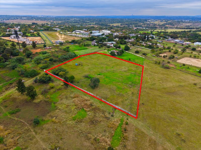 An aerial view of a vacant residential plot of land, clearly demarcated with perimeter fencing, situated in a semi-rural residential area.