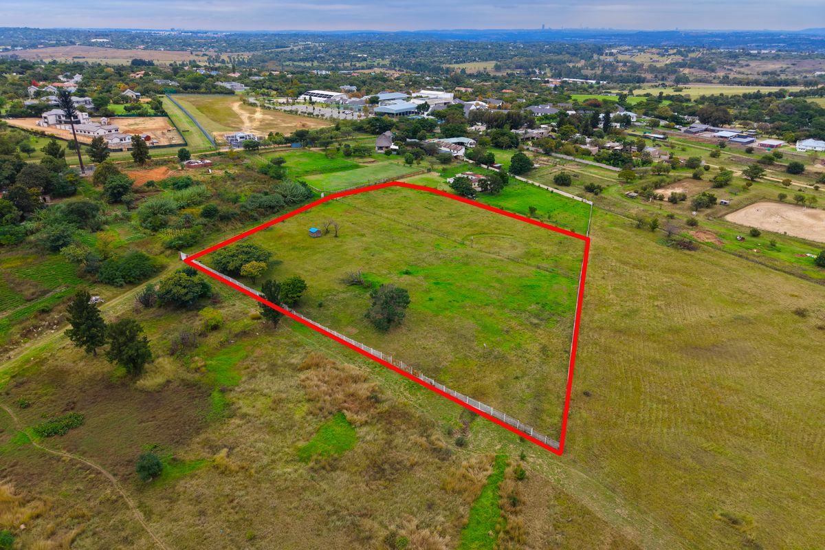 An aerial view of a vacant residential plot of land, clearly demarcated with perimeter fencing, situated in a semi-rural residential area.