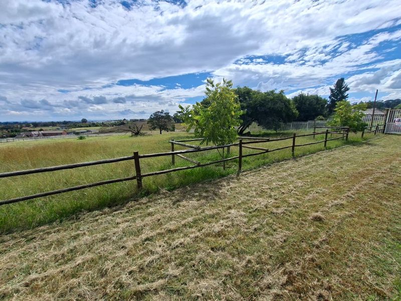 A view of a vacant residential plot featuring established trees and timber post and rail boundary fencing.