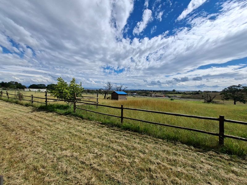 Expansive vacant residential land featuring timber post and rail fencing and a small storage shed, set against a scenic rural landscape.