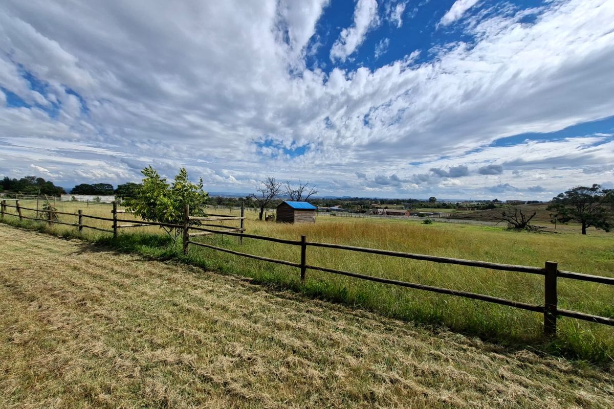 Expansive vacant residential land featuring timber post and rail fencing and a small storage shed, set against a scenic rural landscape.