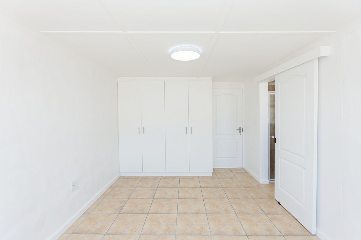 A clean, empty bedroom featuring neutral tiled flooring, built-in white cupboards, and a sliding door leading to an adjacent space.