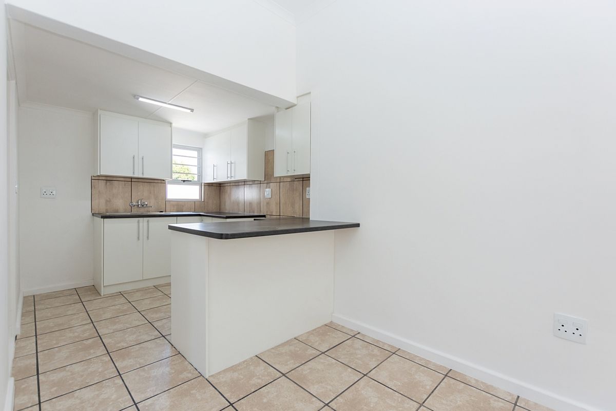 A clean, functional kitchen featuring white cabinetry, dark laminate countertops, a tiled backsplash, and a convenient breakfast bar, finished with neutral ceramic floor tiles.