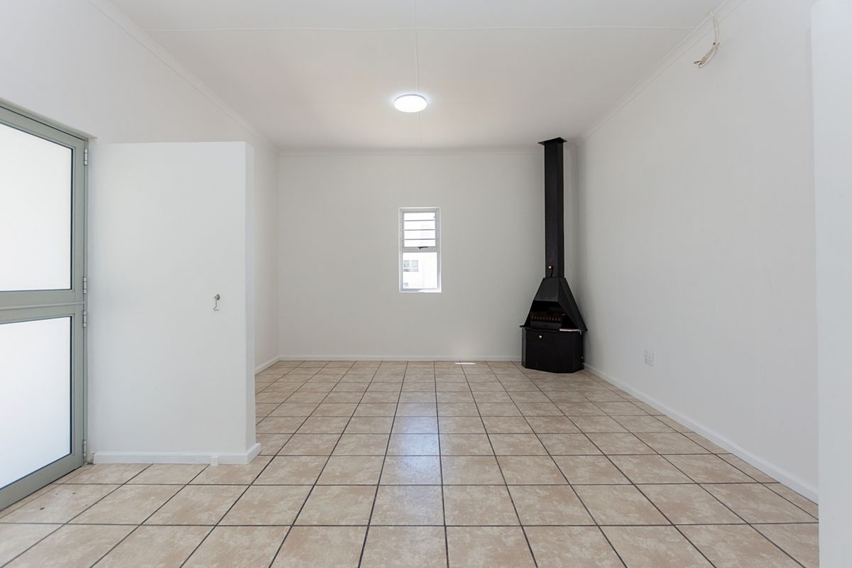 An empty living room featuring tiled flooring, a freestanding fireplace, and a glass panel door leading to the exterior.