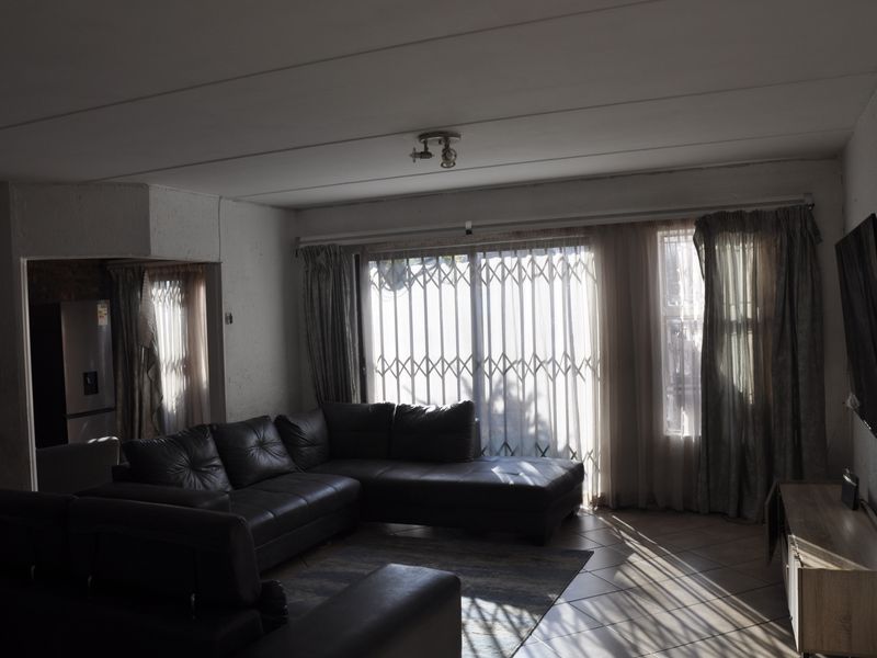 A living room featuring tiled flooring and a sliding glass door with a security gate, providing access to the exterior.