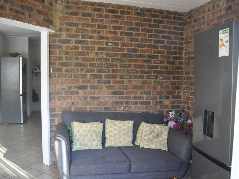 A living area featuring a prominent exposed brick feature wall and tiled flooring, with an open doorway leading to an adjacent room.
