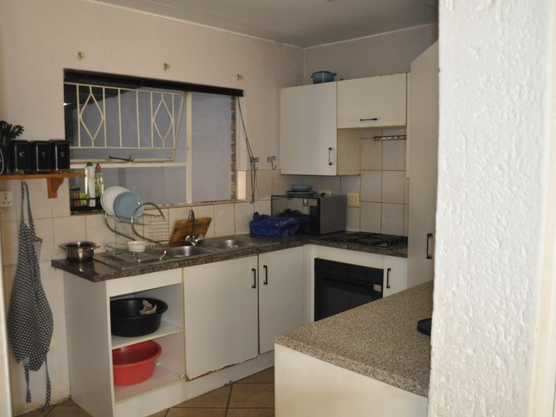 A compact kitchen featuring laminate countertops, built-in cabinetry, a hob, and an oven, with a tiled backsplash and window security bars.