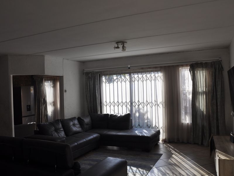 A living room featuring tiled flooring and a sliding glass door with a security gate, providing access to the exterior.