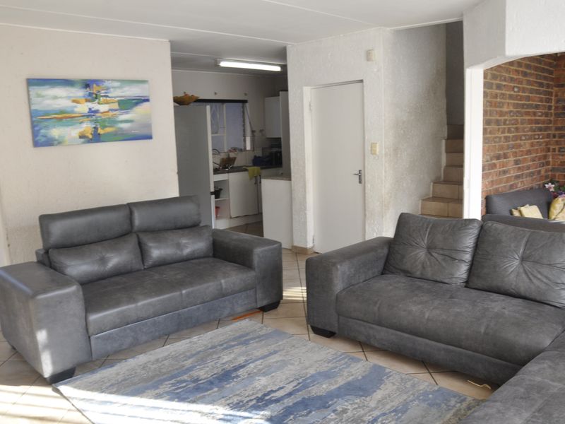 Open-plan living area featuring tiled floors, an exposed brick feature wall, and a staircase, with an adjacent kitchen area visible.