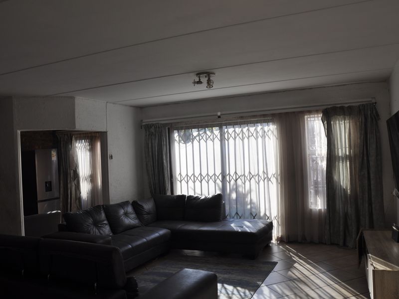A living room featuring tiled flooring, ceiling panels, and a security gate over the sliding door, providing access to the exterior.