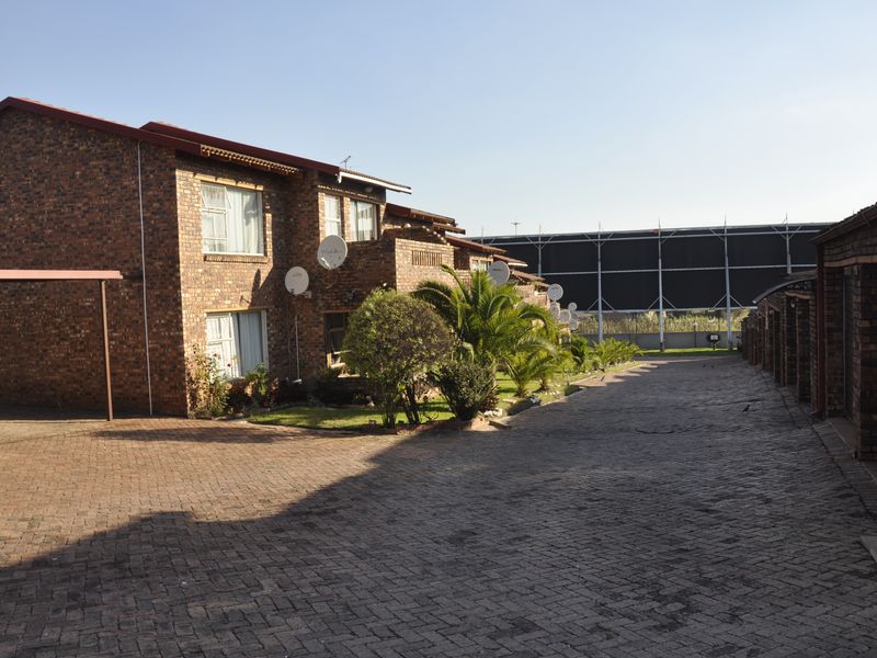Exterior view of a face brick townhouse complex featuring a paved driveway, covered parking, and multiple garage units.